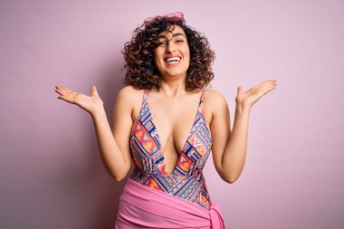 Genç, güzel bir Arap kadın, mayo ve pembe arka planda güneş gözlüğü takmış çılgın ve hayret verici başarısını kutluyor. Kolları havada ve gözleri açık bir şekilde heyecanla haykırıyor. Kazanan konsept