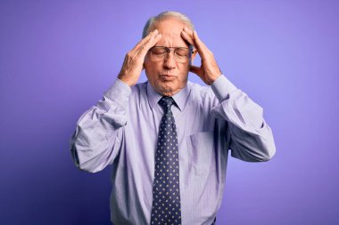 Gri saçlı, gözlüklü, mor izole edilmiş arka planda duran yaşlı bir iş adamı. Başı ağrıyor çünkü stres altında. Migren ağrısı..