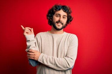 Sakallı, sıradan bir süveter giyen, yüzünde kocaman bir gülümsemeyle kameraya bakan, eli ve parmağı olan genç yakışıklı bir adam..