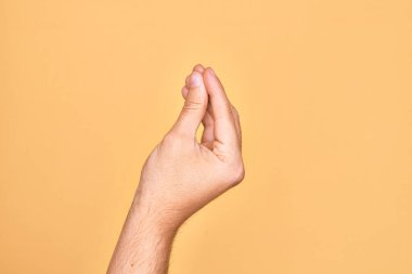 Kafkas genci parmaklarını izole edilmiş sarı arka planda gösteriyor. Parmaklarıyla İtalyan hareketi yapıyor. İletişim hareketi.