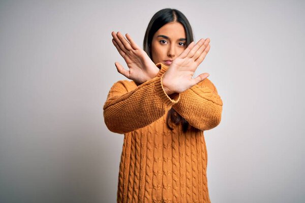 Young beautiful brunette woman wearing casual sweater over isolated white background Rejection expression crossing arms and palms doing negative sign, angry face