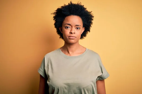 カジュアルなTシャツを着て巻き毛を持つ若い美しいアフリカ系アメリカ人アフロ女性顔に深刻な表情でリラックスしてください シンプルで自然なカメラを見て — ストック写真