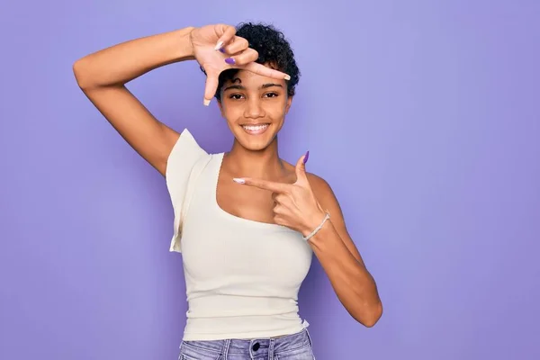 紫色の背景にカジュアルなTシャツを着た若い美しいアフリカ系アメリカ人アフロ女性は 幸せな顔をした手と指でフレームを作り笑顔 創造性と写真の概念 — ストック写真