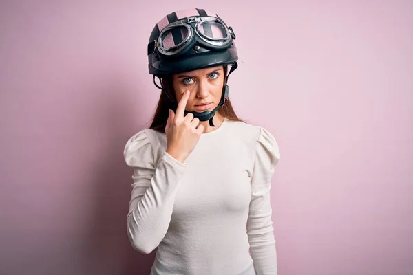 若いです美しいですオートバイの女性とともに青い目ピンクの背景の上に元ヘルメットを身に着けていますあなたのジェスチャーを見ます 疑わしい式 — ストック写真