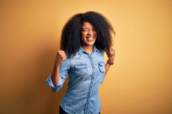 Young beautiful african american woman with afro hair standing over yellow isolated background excited for success with arms raised and eyes closed celebrating victory smiling. Winner concept.