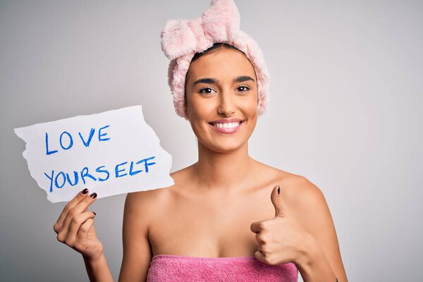 Молодая красивая брюнетка женщина держит бумагу с любовью себя сообщение после душа счастливы с большой улыбкой делает хорошо знак, палец вверх пальцами, отличный знак
