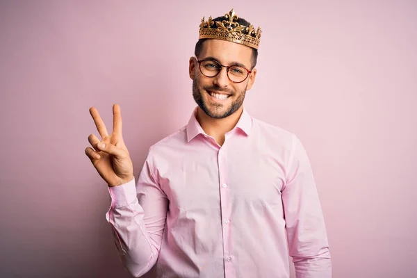 年轻英俊的商人头戴金色王冠 身披粉色背景的王冠 喜形于色地微笑着 在镜头前眨眼示意胜利 第二点 — 图库照片
