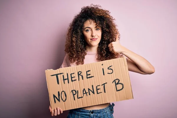 Young beautiful activist woman with curly hair and piercing protesting asking for change planet happy with big smile doing ok sign, thumb up with fingers, excellent sign