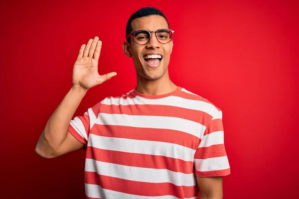 若いハンサムなアフリカ系アメリカ人男性カジュアルなストライプのTシャツと眼鏡を身に着けているこんにちは幸せと笑顔 優しい歓迎ジェスチャー — ストック写真