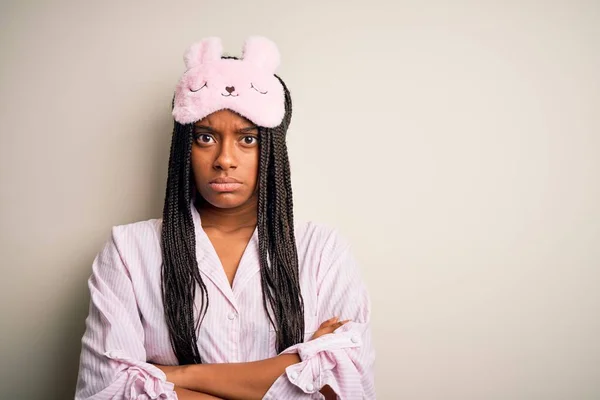年轻的非洲裔美国女人 身穿粉色睡衣 戴着睡眠面罩 面对孤立的背景 怀疑和紧张 双手交叉 脸上露出不赞成的表情 消极的人 — 图库照片