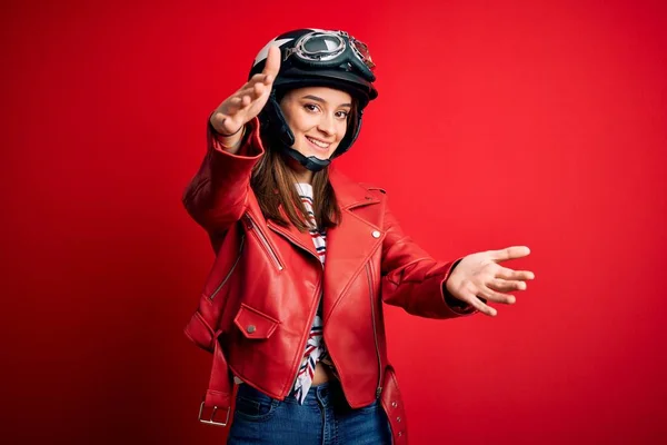 若い美しいブルネットのオートバイのヘルメットと抱擁のためのオープン腕で笑顔カメラを見て赤いジャケットを身に着けているオートバイの女性 幸せを受け入れる陽気な表情 — ストック写真