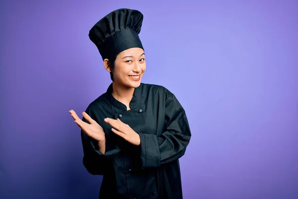 年轻美丽的中国厨师女士身穿炊具制服 头戴紫色背景的帽子 拍手喝彩 欢快快乐 自豪地携手共进 — 图库照片