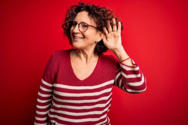 Orta yaşlı güzel kıvırcık saçlı kadın kırmızı arka planda sıradan çizgili süveter giyiyor. Kulağı kulağında bir söylenti ya da dedikoduyu dinliyor. Sağırlık kavramı.