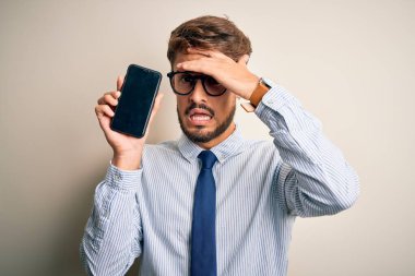 Akıllı telefonu elinde tutan genç işadamı, izole edilmiş beyaz arka planda, elleri başının üstünde, utanç ve şaşkınlık dolu, sinirli ve hayal kırıklığına uğramış bir şekilde duruyor. Hata için korku ve üzüntü.