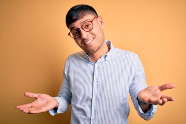 Sarı arka planda inek gözlüğü takan yakışıklı İspanyol iş adamı. Kolları ve elleri havada, kafası karışmış bir ifade. Şüphe kavramı.