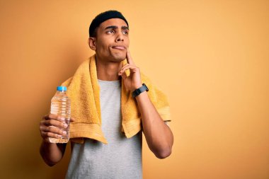 Yakışıklı Afro-Amerikan sporcusu havluyla su içiyor. Ciddi bir yüz ifadesi var. Soru sormayı düşünüyor.