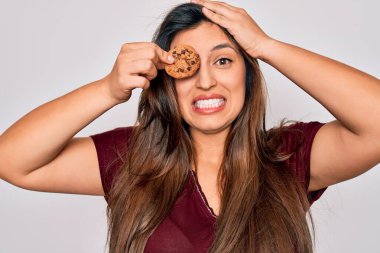Young hispanic woman eating sweet chocolated chips cookie over isolated background stressed with hand on head, shocked with shame and surprise face, angry and frustrated. Fear and upset for mistake. clipart