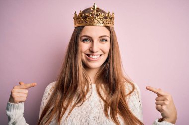 Genç, güzel, kızıl saçlı, kraliçe tacı takan, pembe arka planda kendine güvenen, yüzünde bir gülümsemeyle, gururlu ve mutlu bir şekilde kendini gösteren bir kadın..