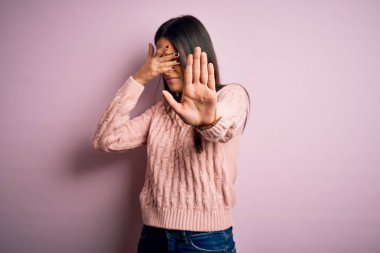 Genç, güzel, esmer bir kadın, pembe arka plan üzerine günlük süveter giyip, gözlerini ellerle kapatıyor ve üzgün ve korku ifadeleriyle jest yapıyor. Utanç verici ve olumsuz bir kavram..