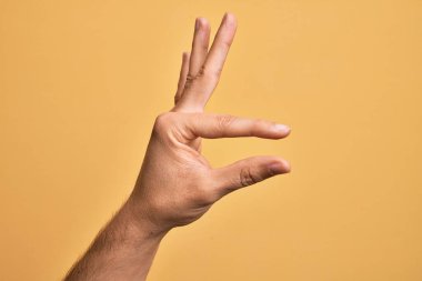 İzole edilmiş sarı arka plan üzerinde parmaklarını gösteren beyaz bir adamın eli. Görünmez bir şeyi alıp, parmaklarıyla uzayı gösteren bir nesneyi tutuyor.
