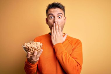 Fıstıklı genç adam, izole edilmiş sarı arka planda duruyor. Ağzı kapalı, elleri utançla kaplı, korkunun ifadesi, sessizlikten korkmak, gizli bir konsept.