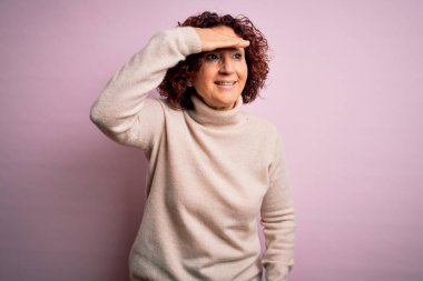 Orta yaşlı, kıvırcık saçlı, pembe arka plan üzerine balıkçı yaka kazak giyen çok mutlu ve tebessüm eden güzel bir kadın. Konsept aranıyor.