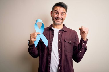 Genç yakışıklı adam mavi kanser kurdelesini soyutlanmış beyaz arka planda tutuyor gururla bağırıyor, zaferi ve başarıyı kutluyor çok heyecanlı, coşkulu bir duygu.