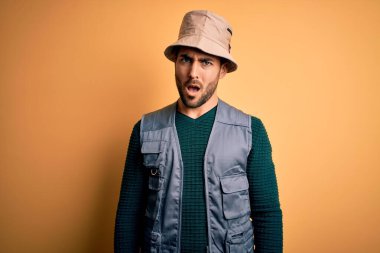 Tatilde sakallı yakışıklı turist sarı arka planda kaşif şapkası takıyor. Şok olmuş, şüpheci ve alaycı görünüyor.