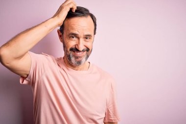 İzole edilmiş pembe arka plan kafa karışıklığı ve soru soran günlük tişört giyen orta yaşlı beyaz bir adam. Şüpheyle kararsız, kafa kafaya düşünerek. Düşünceli kavram.
