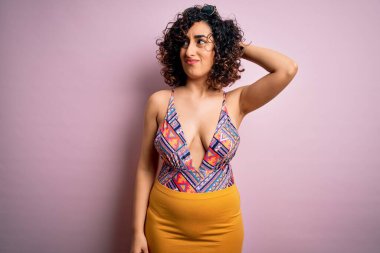 Tatilde olan genç, güzel bir Arap kadın. Pembe arka planda mayo ve güneş gözlüğü takıyor. Soruyu merak ediyor. Şüpheyle kararsız, kafa kafaya düşünerek. Düşünceli kavram.