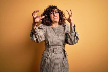 Güzel bir Arap iş kadını. Elbise ve gözlük takıyor. Sarı arka planda duruyor.