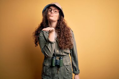 Gezgin şapkası ve dürbünle kameraya bakıp havada öpücükler saçan genç ve güzel bir turist kadın güzel ve seksi. Aşk ifadesi.