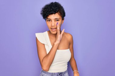 Genç ve güzel Afro-Amerikan kadın mor arka plan üzerine gündelik tişört giyip gizli dedikodular söylüyor, kötü niyetli konuşmalar fısıldıyor.