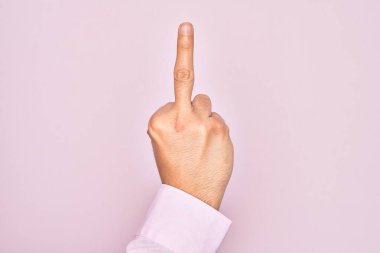Hand of caucasian young man showing fingers over isolated pink background showing provocative and rude gesture doing fuck you symbol with middle finger