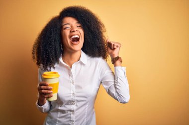 Afro saçlı, kahve fincanından kahve içen, gururla bağıran, zaferi ve başarıyı kutlayan heyecanlı, neşeli Amerikalı genç iş kadını.