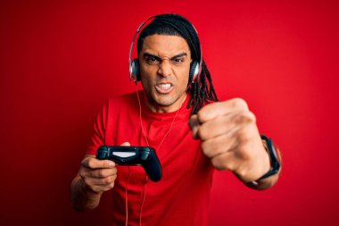 Rastalı Afrikalı Amerikalı adam joystick ve kulaklıkla video oyunu oynuyor sinirlenmiş ve sinirlenmiş bağırıyor, çıldırmış ve el kaldırarak bağırıyor, öfke kavramı
