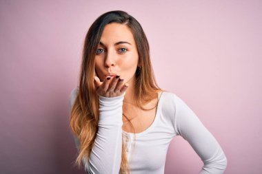 Genç, sarışın, mavi gözlü, pembe arka planda beyaz tişörtlü, güzel bir kadın. Kameraya bakıp havada el sallayan bir öpücük veriyor. Güzel ve seksi. Aşk ifadesi.