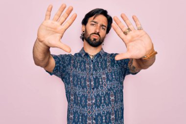 Pembe arka planda hippi tarzı giyinmiş, elleri ve parmakları kullanarak çerçeve yapan genç, İspanyol bohem bir adam.