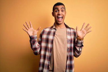 Sarı arka planda dikilen rahat gömlekli genç ve yakışıklı Afro-Amerikan erkeği çılgın ve başarısını kutlarken kollarını kaldırmış ve gözleri açık bir şekilde heyecanla haykırıyordu. Kazanan konsept