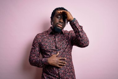 Genç, yakışıklı, Afro-Amerikalı bir adam pembe arka planda dikiliyor. Hastalık, ateş, grip ve soğuk algınlığı için alnına dokunuyor.