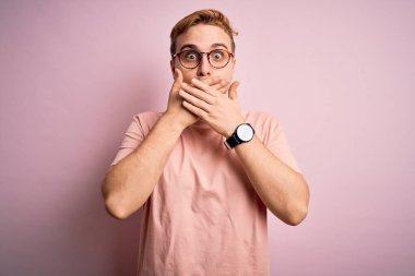 Genç, kızıl saçlı, günlük tişört giyen, izole edilmiş pembe arka planda duran, ağzı yanlışlıkla ellerle kapatan genç bir adam. Gizli konsept.