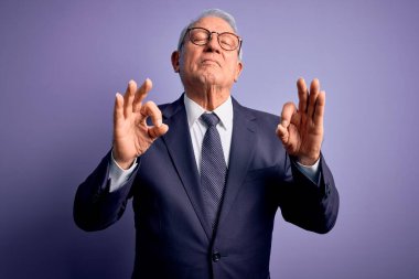 Gri saçlı, gözlüklü, şık takım elbiseli, mor arka planda kravat takan, gözleri kapalı, meditasyon yaparken parmaklarıyla gülümseyen yaşlı iş adamı. Yoga konsepti.