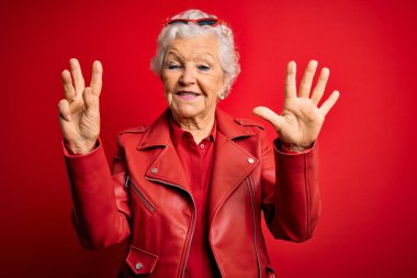 Son sınıf güzeli, gri saçlı, günlük kırmızı ceket giyen, güneş gözlüklü, 8 numaralı parmaklarıyla işaret eden, kendinden emin ve mutlu bir kadın..