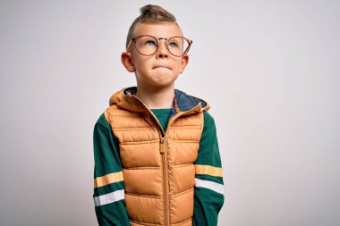 Mavi gözlü, kışlık paltolu ve gözlüklü genç beyaz bir çocuk gülümsüyor ve yan tarafa bakıyor ve düşünüyor..