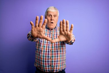 Kıdemli yakışıklı, beyaz gömlekli, soyutlanmış mor arka planda, avuçlarıyla jestleri durduran, sinirli ve hüsran dolu bir adam.