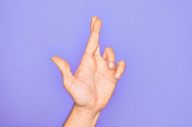 İzole edilmiş mor arka plan üzerinde parmaklarını gösteren beyaz bir gencin eli. Parmakları çapraz, batıl inançlar ve şanslı bir jest, şanslı ve umut dolu bir ifade.