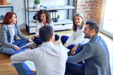 Bir grup iş adamı mutlu ve kendinden emin gülümsüyor. Yerde oturup rahatlamak birlikte çalışmak, konuşmak ve ofiste belgeleri okumak.