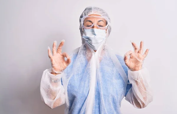 白い背景の上に保護コロナウイルス装置を身に着けている中年の看護師の女性はリラックスし 指で瞑想ジェスチャーを行う目を閉じて笑顔 ヨガのコンセプト — ストック写真