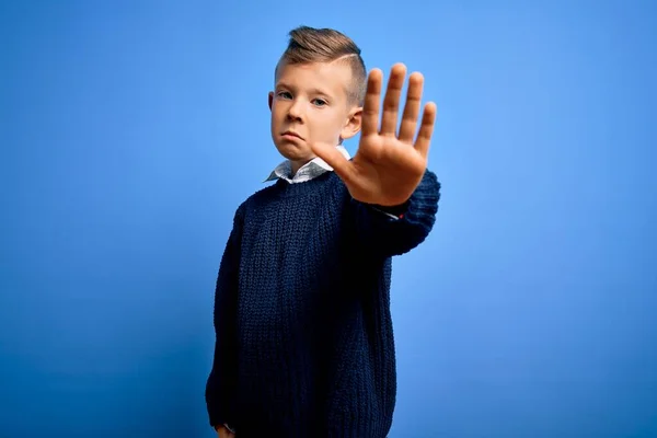 青い背景に冬のセーターを着た青い目の若い白人の子供は 手の手のひらで歌うのをやめます 顔に負と深刻なジェスチャーで警告式 — ストック写真