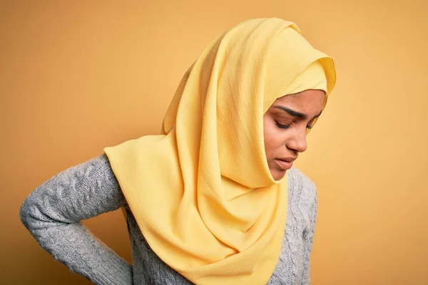 Young beautiful african american girl wearing muslim hijab over isolated yellow background Suffering of backache, touching back with hand, muscular pain